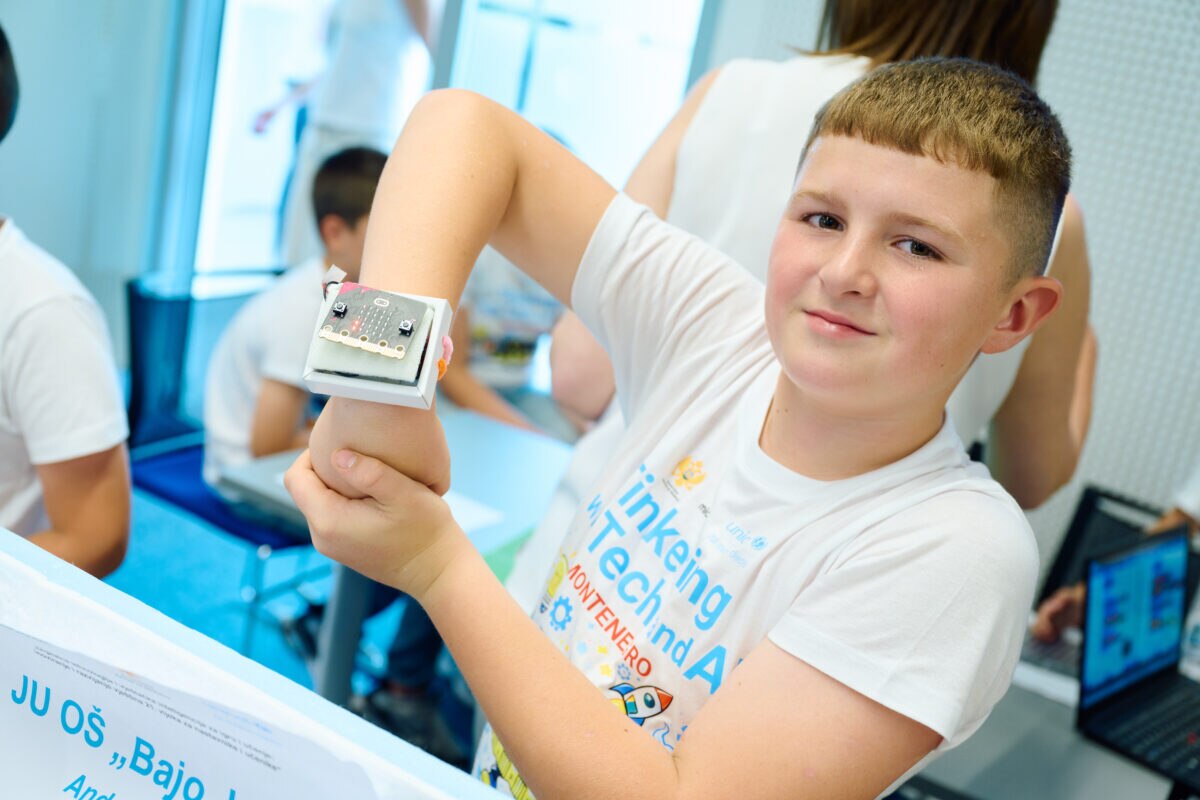 A boy shows a small programmable device attached to his arm during a hands-on technology activity.