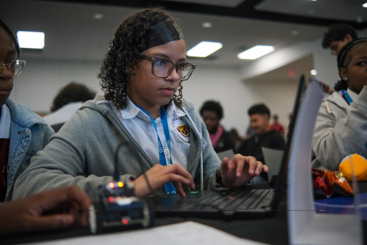 Student working on a laptop with a small robotic vehicle during Arm's Drive the Future 2026 STEM workshop.