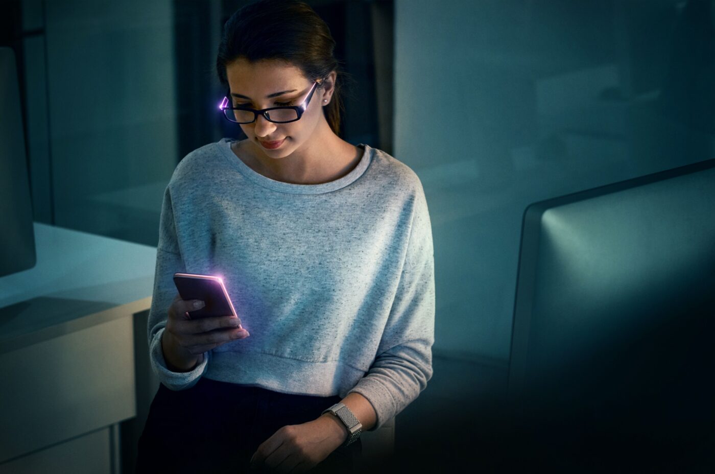 Woman wearing smart glasses and a smartwatch while using a smartphone, illustrating AI-powered wearable technology.